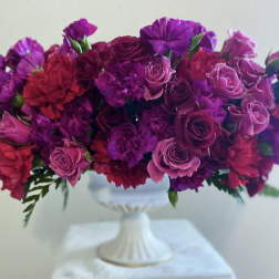 Purple and pink floral arrangement in a white pedestal vase