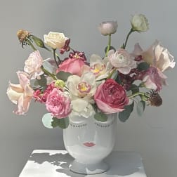 Pink and white flower arrangement in a white face vase