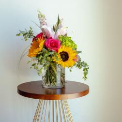 Mixed bouquet in a clear glass vase with sunflowers, roses, and lilies