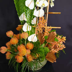 Tropical floral arrangement with white orchids and orange blooms in a low vase