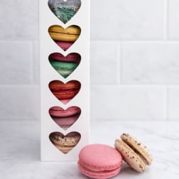 Box of assorted heart-shaped macarons with two macarons in front