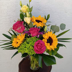 Bouquet of pink roses, yellow sunflowers, and green hydrangea in a glass vase