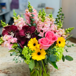 Mixed bouquet with pink roses, yellow daisies, and dark orchids in a glass vase