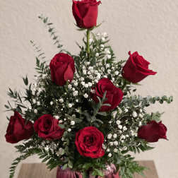 Red roses arranged in a pink glass vase with white filler flowers