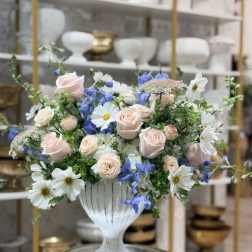 Pastel bouquet of pink roses, white daisies, and blue flowers in a white vase