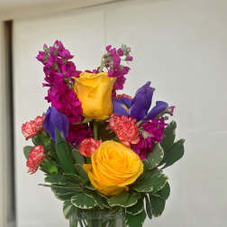 Colorful bouquet of yellow roses, purple irises, and pink flowers in a glass vase