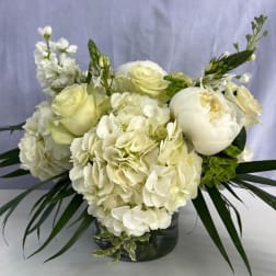 Low white arrangement of hydrangeas, roses, and peonies in a clear glass vase