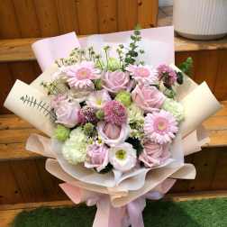 Bouquet of pink roses, gerbera daisies, and mixed blooms wrapped in pastel paper
