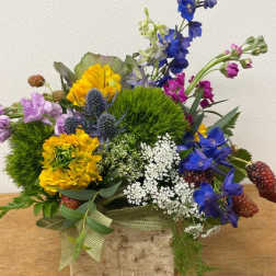 Colorful arrangement of blue, yellow, and purple flowers in a rustic birch container