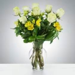 Glass vase of white roses and yellow alstroemeria in a rounded mixed bouquet