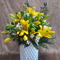 Yellow lilies and white flowers arranged in a white textured vase