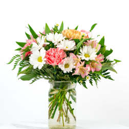 Mixed bouquet of white daisies, pink carnations, and peach blooms in a clear glass jar vase