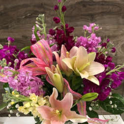 Pink and cream lilies with purple flowers in a glass vase