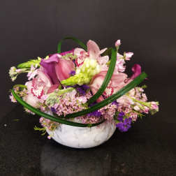 Pink and purple floral arrangement in a white bowl vase