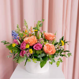 Mixed bouquet of peach, pink, and yellow flowers in a white vase