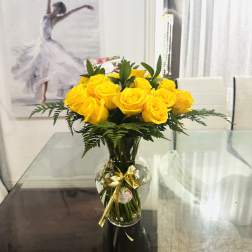 Yellow roses in a glass vase with a gold ribbon