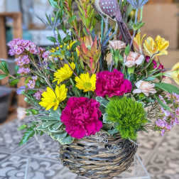 Mixed flower arrangement in a woven basket with a decorative bird