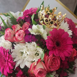 Hand-tied bouquet of pink roses and gerbera daisies with white blooms and a small gold crown accent.