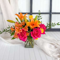 Bouquet of pink roses, orange lilies, and yellow blooms in a glass vase