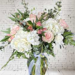Large bouquet of pink and white flowers in a glass vase with a ribbon