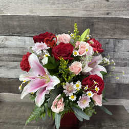 Bouquet of red roses, pink lilies, and small daisies in a red vase
