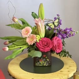 Pink roses and lilies in a square vase with a butterfly accent