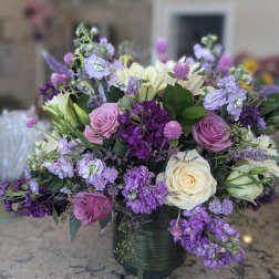 Large arrangement of purple, lavender, and cream flowers, including roses and stock, in a green vase