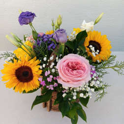 Mixed bouquet with sunflowers, pink rose, and purple lisianthus in a rustic basket