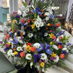 Colorful spring wreath and matching arrangement with irises, tulips, daffodils, and daisies in a circular design.
