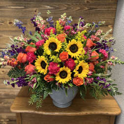 Mixed bouquet with sunflowers, orange roses, and purple flowers in a gray vase