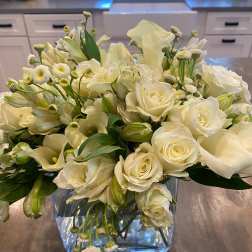 White roses and calla lilies arranged in a clear square vase