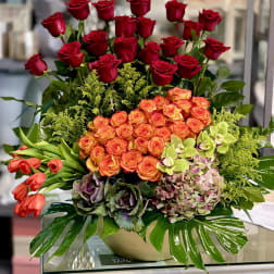 Mixed bouquet of red and orange roses with orchids in a low vase