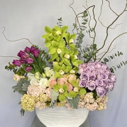 Mixed floral arrangement in a white rectangular vase with orchids and roses