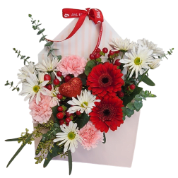 Envelope-shaped pink box filled with red gerbera daisies, white daisies, pink carnations, and a red glitter heart pick.