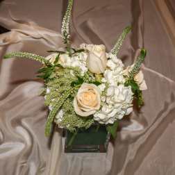 Small wedding centerpiece of ivory roses and white hydrangeas in a glass cube vase
