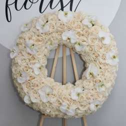 Cream rose wreath with white orchid accents on a wooden easel
