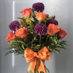 Bouquet of orange roses and purple pompon flowers in a glass vase with an orange bow