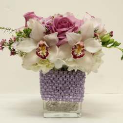 Pink roses and white orchids in a clear square vase with a purple wrap