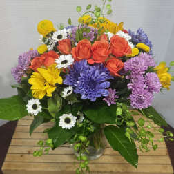 Mixed bouquet of orange roses, purple chrysanthemums, and yellow flowers in a glass vase