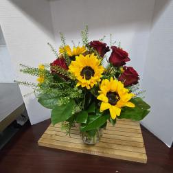 Bouquet of red roses and yellow sunflowers in a clear glass vase