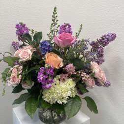 Mixed bouquet of pink, purple, and peach flowers in a glass vase