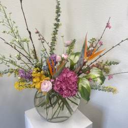 Mixed floral arrangement in a round glass vase with pink, yellow, purple, and orange blooms