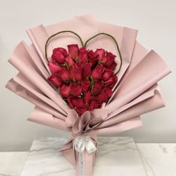 Heart-shaped bouquet of red roses wrapped in pale pink paper