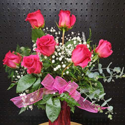 Pink roses arranged in a tall pink vase with baby's breath and ribbon