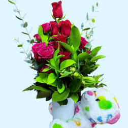 Bouquet of red roses in a white vase with a colorful teddy bear