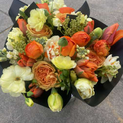 Bouquet of orange, cream, and pale yellow flowers wrapped in black paper