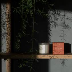Candle in a glass jar beside its orange box on a wooden shelf