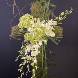 Cross-shaped floral arrangement with white lilies, green hydrangeas, and orchids