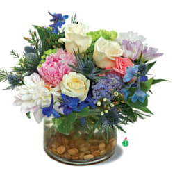 Low glass vase filled with cream roses, pink peony, blue and purple blooms, and mixed pastel flowers.