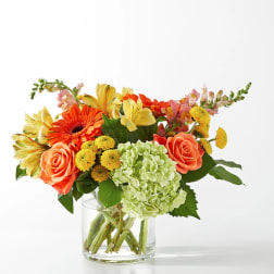 Mixed bouquet of orange, yellow, and green flowers in a clear glass vase